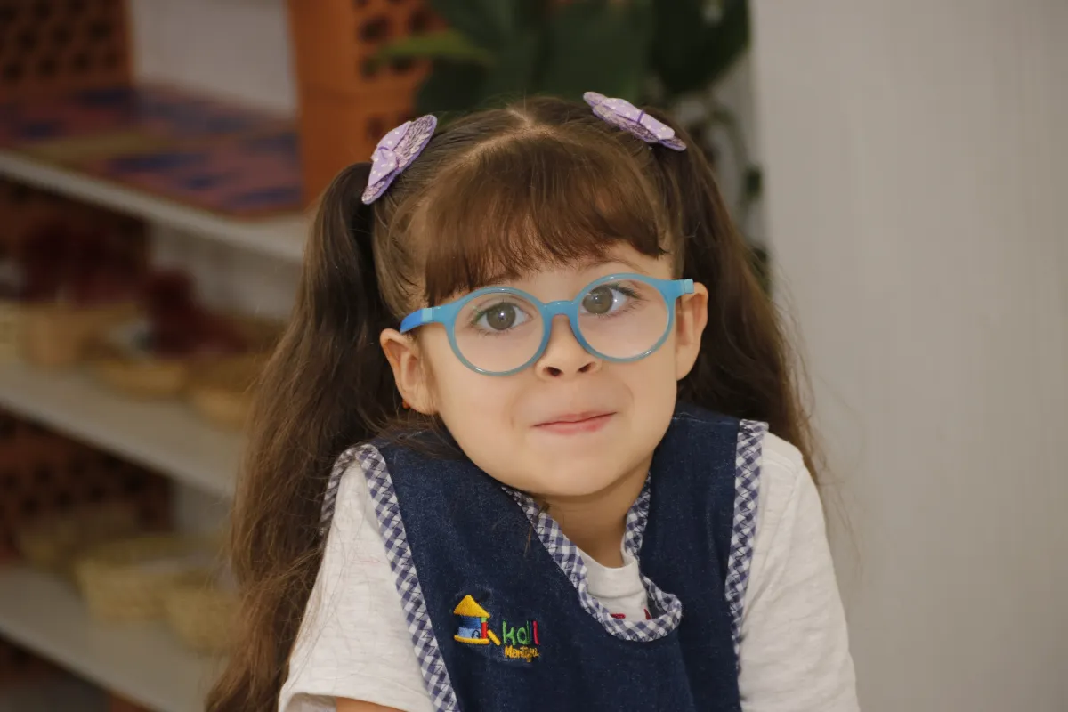 Niña con lentes redondos azules y dos coletas adornadas con moñitos color violeta.